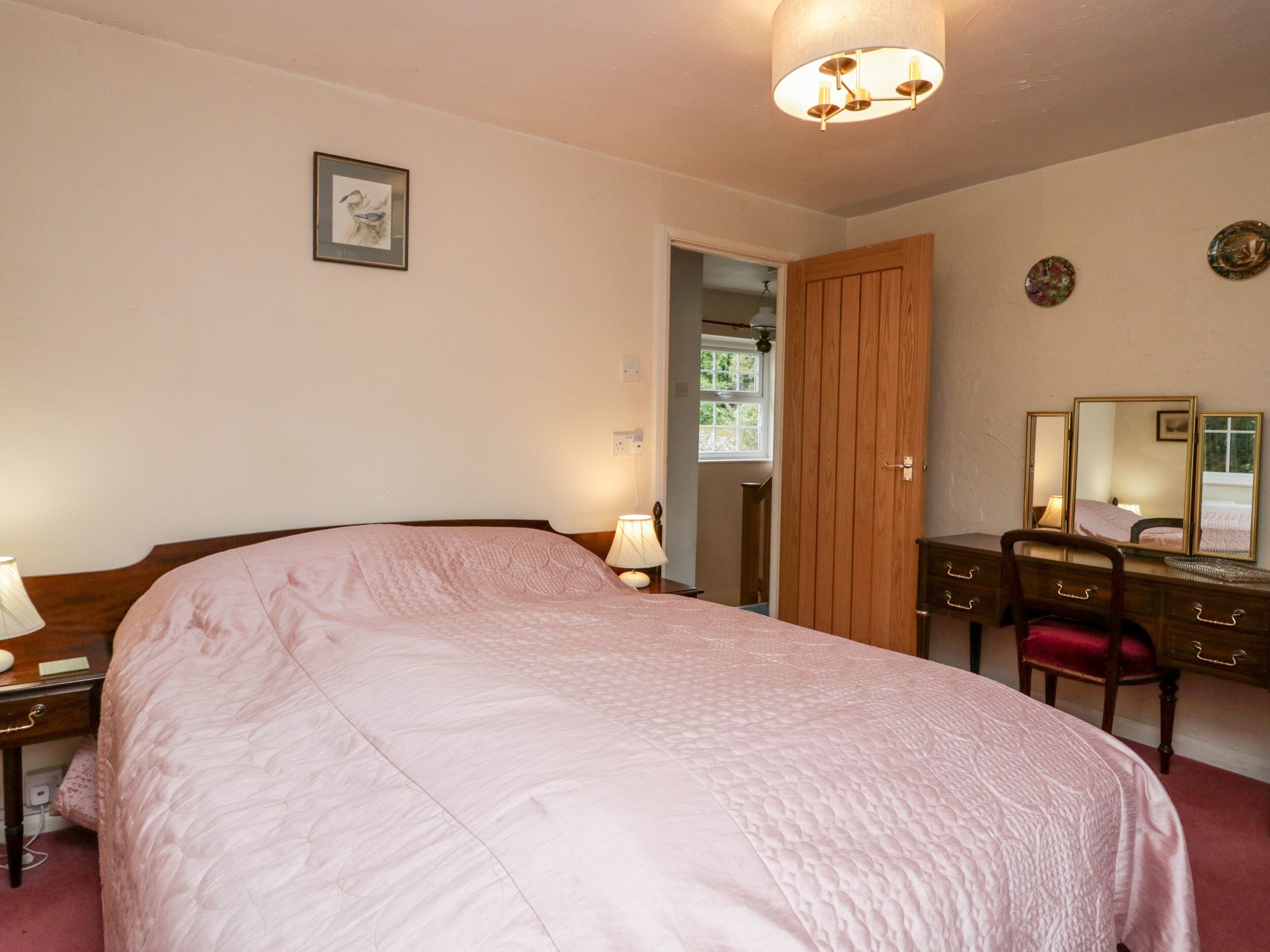 A bedroom with a bed, bedside tables, a dresser, a mirror, and a door leading to another room.