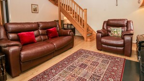 Een woonkamer met een bruine leren bank, een bijpassende fauteuil, een houten trap en een vloerkleed met een patroon.