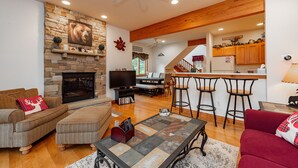 A living room with a stone fireplace, a television, and a cozy seating area. - Cozy Dog Friendly Retreat w/ Hot Tub & Views (McHenry)