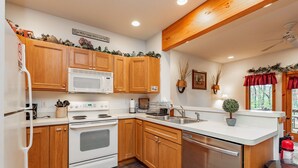 A modern kitchen with wooden cabinets, a stainless steel dishwasher, and a white microwave. - Cozy Dog Friendly Retreat w/ Hot Tub & Views (McHenry)