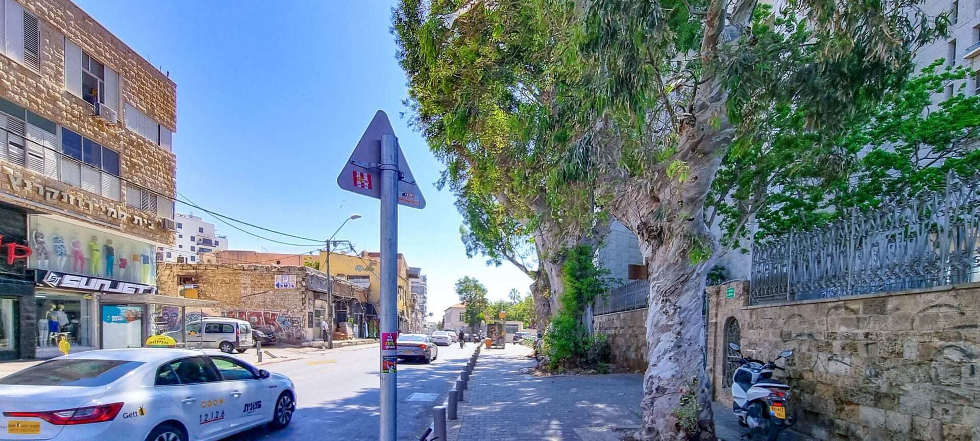 Una calle con un coche blanco, una acera arbolada y una pared de piedra.