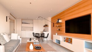 A modern living room with a sofa, coffee table, and TV. There is a kitchen area with cabinets and a dining table. - Blanche Eilat (Tel Aviv)