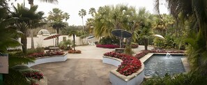 Un jardin aménagé avec une piscine, des palmiers et des espaces de détente en plein air.