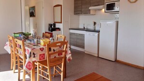 A compact kitchen with a microwave, refrigerator, and a dining area with a table set for four. - Equipped apartment in Superdévoluy (Le Devoluy)