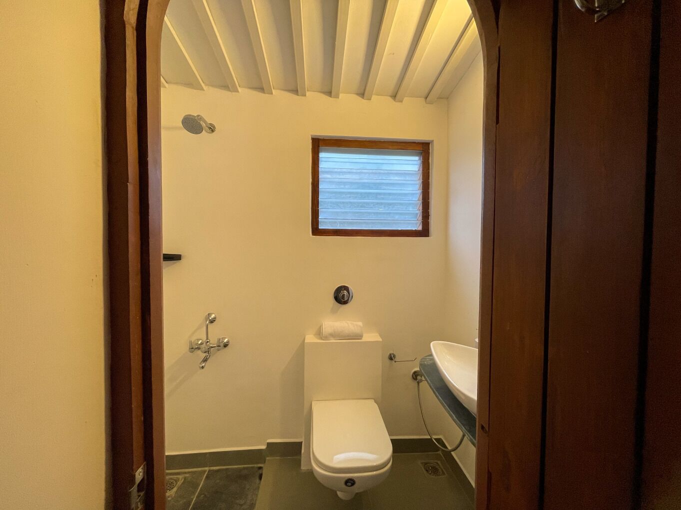 Un baño pequeño y funcional con inodoro, lavamanos y ventana sobre el inodoro.