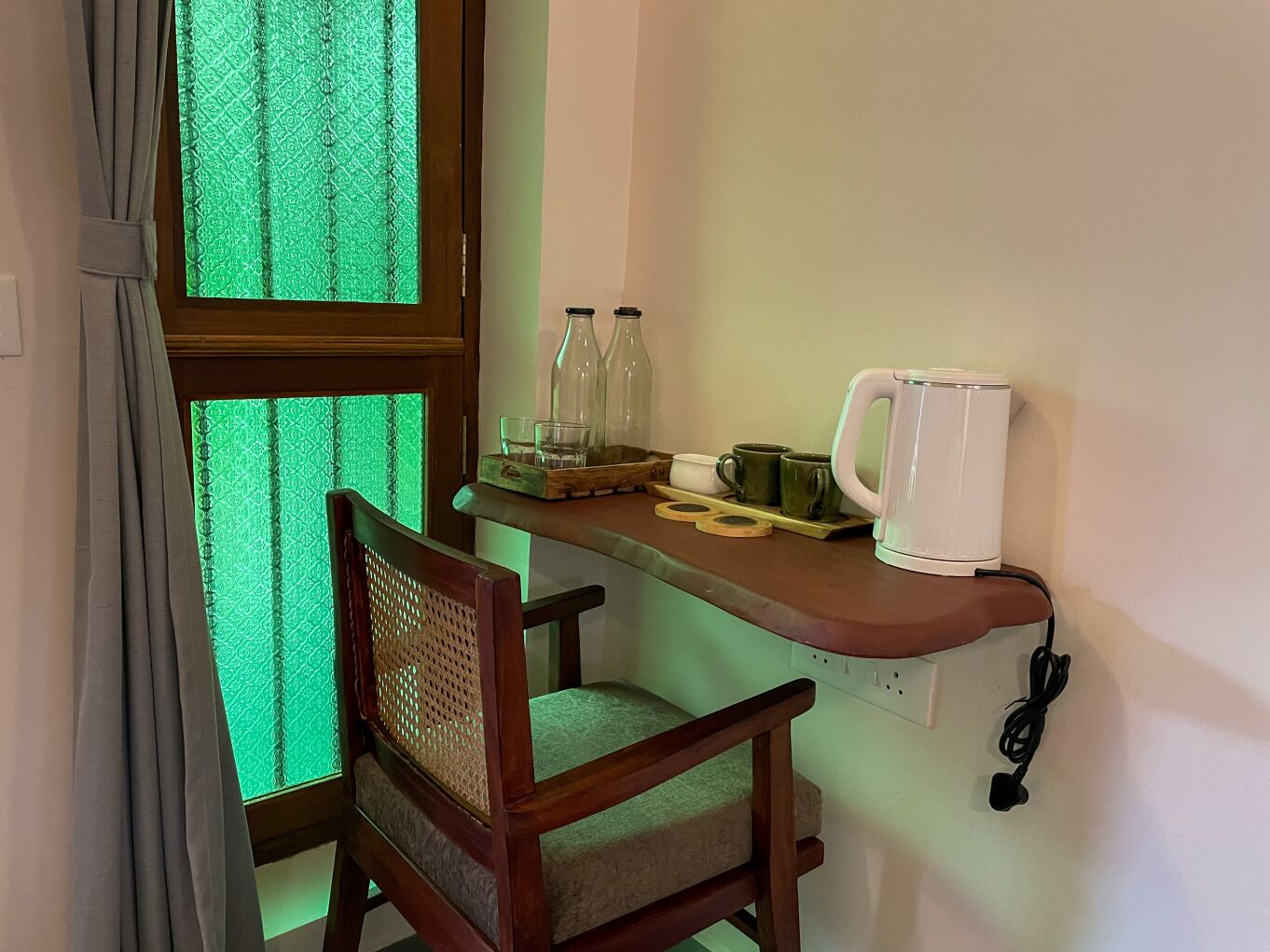 Une petite cuisine équipée avec une table en bois, une chaise et une fenêtre ornée de rideaux à motifs verts.