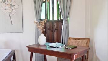 A room with a wooden table, a chair, a laptop, a notebook, and a vase with dried flowers.