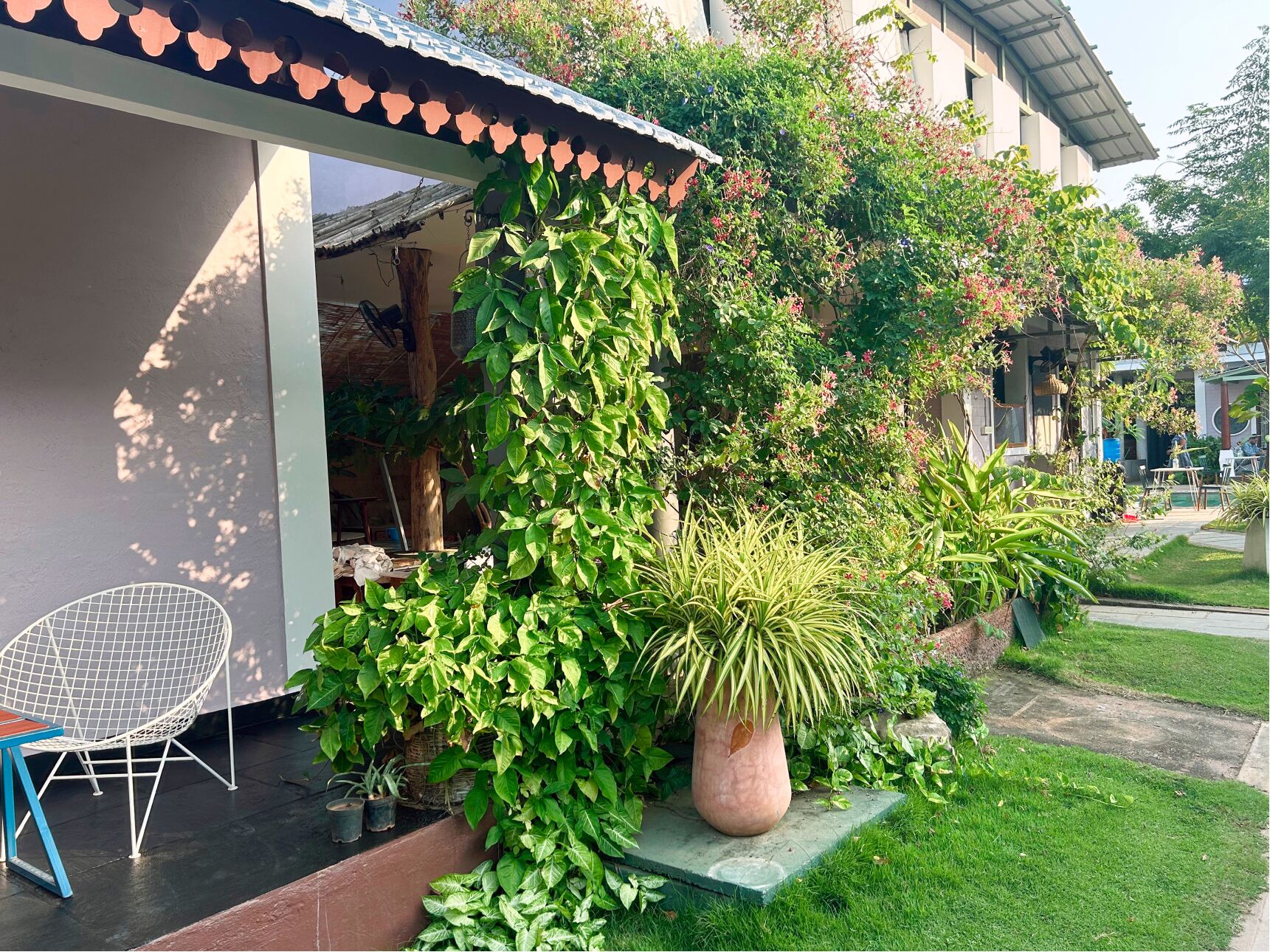 Un edificio moderno con un área de estar cubierta al aire libre, rodeado de abundante follaje y plantas en macetas.