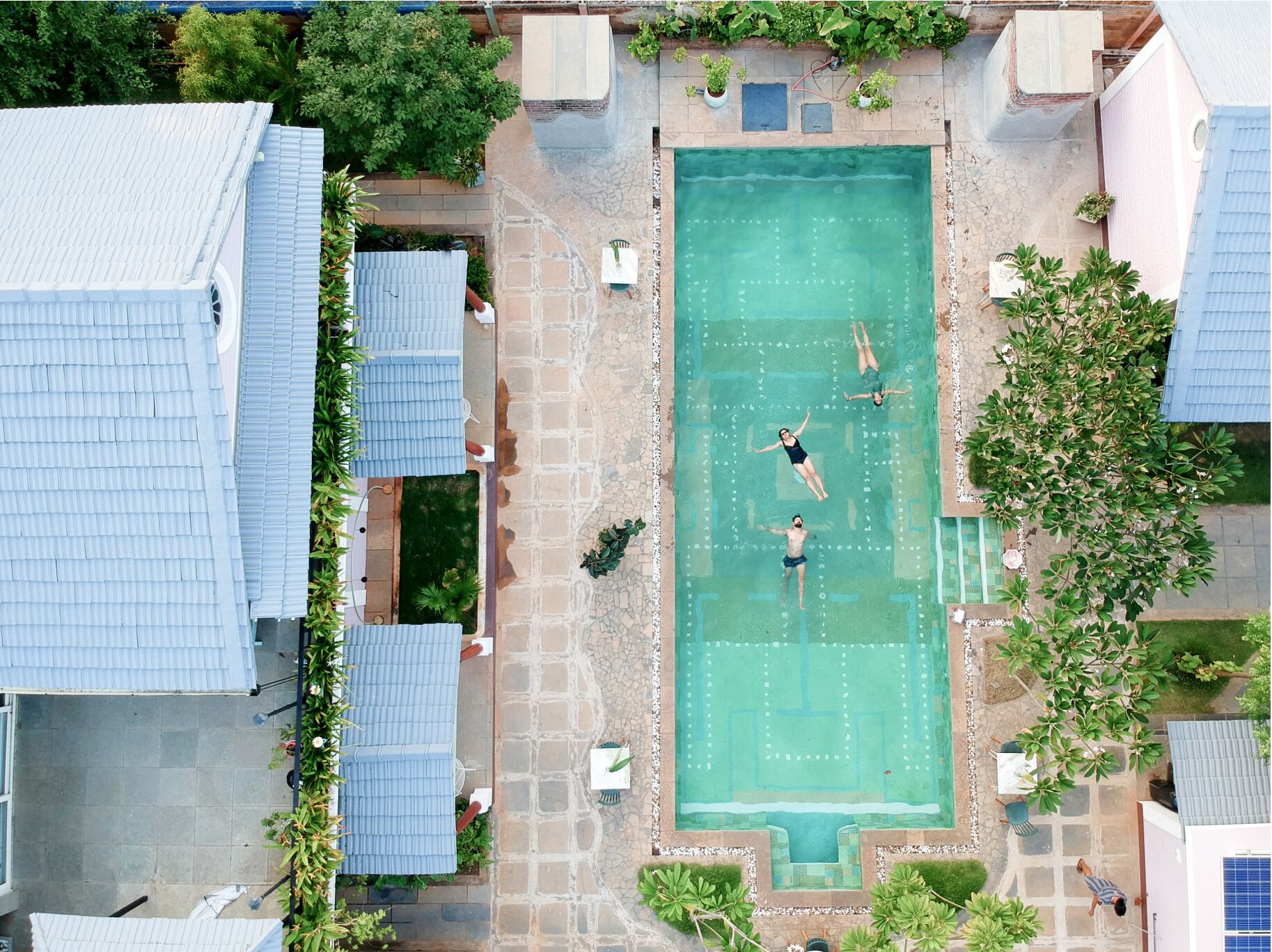 Vista aérea de una piscina rodeada de baldosas de piedra, con algunas personas nadando.
