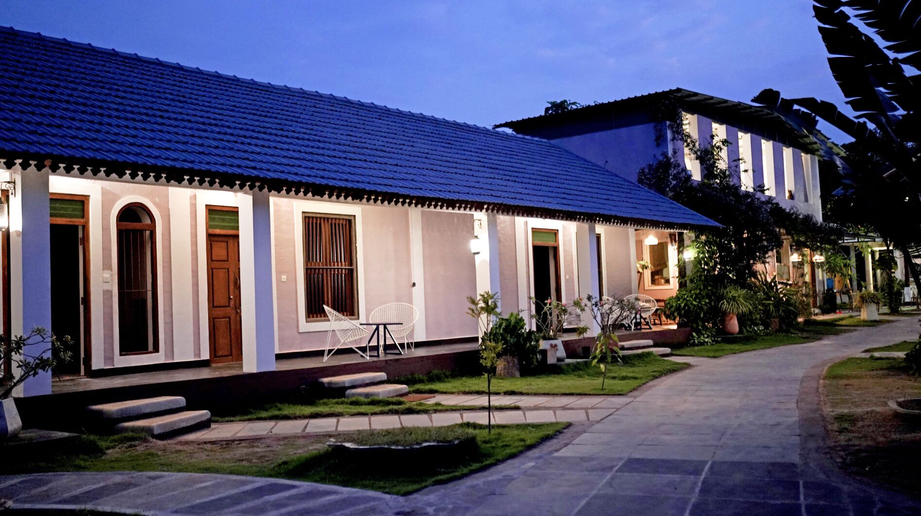 A two-story house with a tiled roof, a front porch with chairs, and a well-maintained garden.
