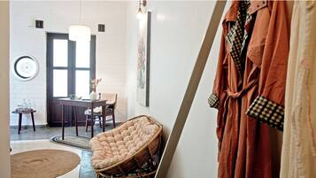 Una habitación con una silla de mimbre, una mesa con un florero y una bata colgada.