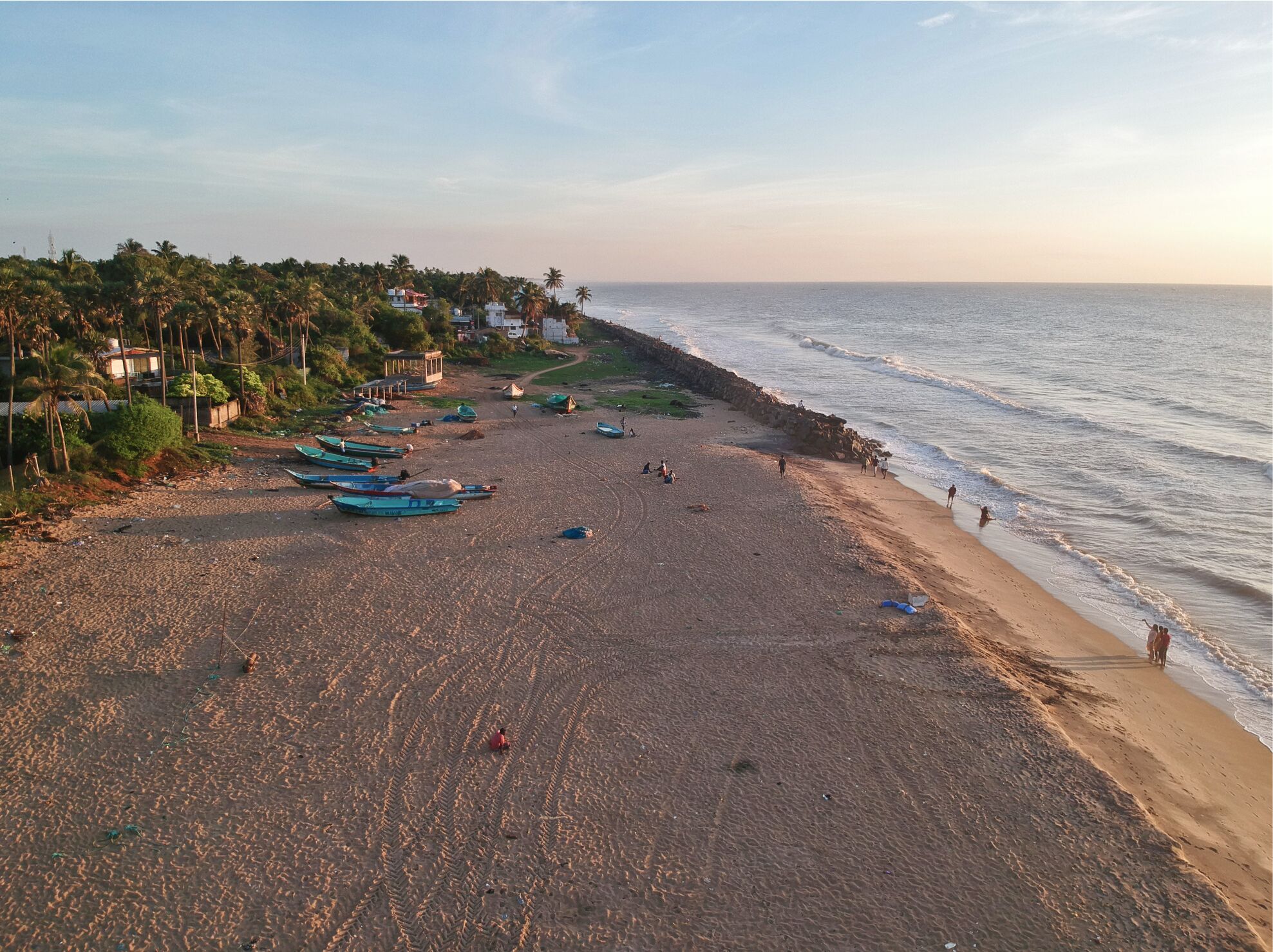 A beach with boats, people, and houses in the background.