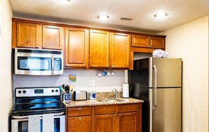 Kitchen features a microwave, stove, refrigerator, and sink with a faucet, along with ample storage in the cabinetry.