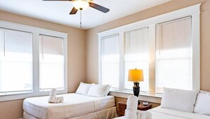 Two beds with crisp linens, a bedside table, and a large window with blinds.