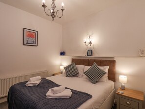 Una cama bien tendida con una manta azul y dos toallas, una mesita de noche de madera con una lámpara, un cuadro colgado en la pared y un candelabro.