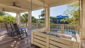 Un espacio de estar al aire libre techado con vista a la piscina, terraza de madera y mecedoras.