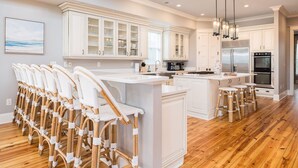 Una cocina amplia con muebles blancos, una isla central con taburetes de bar y un refrigerador de acero inoxidable.