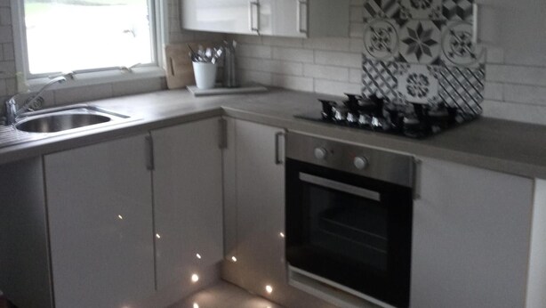 A kitchen with white cabinets, a stainless steel sink, a tiled backsplash, and a stove. - Captivating 1-bed Chalet in Newquay (Newquay)
