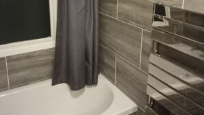 A bathroom with a bathtub, a window with a curtain, and tiled walls. - Captivating 1-bed Chalet in Newquay (Newquay)