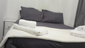 A neatly made bed with a white and dark-colored duvet, two pillows, and a folded white towel on the side. - Captivating 1-bed Chalet in Newquay (Newquay)
