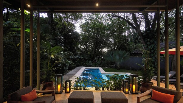 Zona junto a la piscina con sillas de descanso y una mesa, rodeada de exuberante vegetación y vistas despejadas a la piscina.