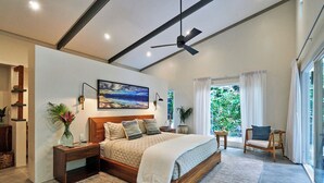Un dormitorio moderno con una cama grande, un ventilador de techo, vista a zonas verdes y una ventana con cortinas.