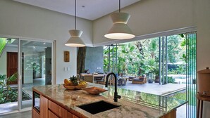 Una cocina moderna con una isla grande, un lavamanos negro e iluminación colgante.
