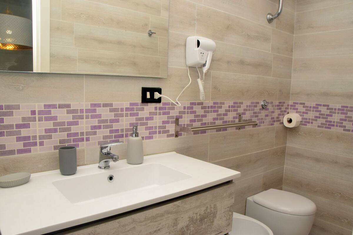 Une salle de bain avec un lavabo blanc, un miroir, un sèche-cheveux et des toilettes.