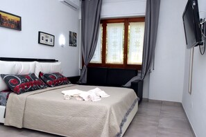 A neatly made bed with a beige cover, a black headboard, and red and black patterned pillows. There are two framed pictures on the wall and a television mounted on the wall. - B&B Royal Reggia di Caserta (Casagiove)