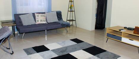 Un salon avec un canapé, un grand lampadaire, un meuble TV en bois et un tapis à motifs.