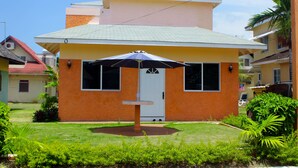 A two-story building with a white door and windows, surrounded by greenery and a small patio area with an umbrella. - Peaceful Retreat (Discovery Bay)