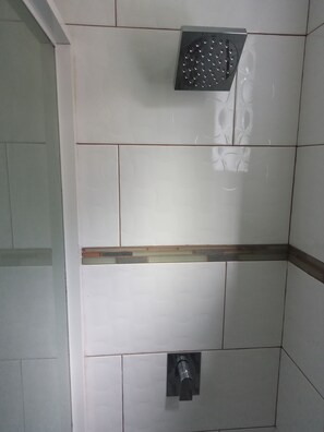 A tiled shower wall with a handheld showerhead and a wall-mounted faucet.
