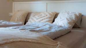 Ein Bett mit weißem Kopfteil, mehreren Kissen und einer beigen Decke.