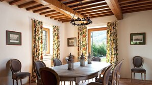Un comedor con una mesa redonda, seis sillas, cortinas con motivos florales y una lámpara de araña.