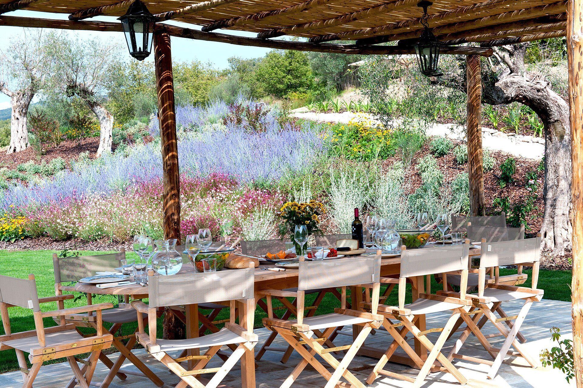Un espace de restauration en plein air agrémenté d’une pergola, de chaises en bois et d’une table dressée pour un repas.