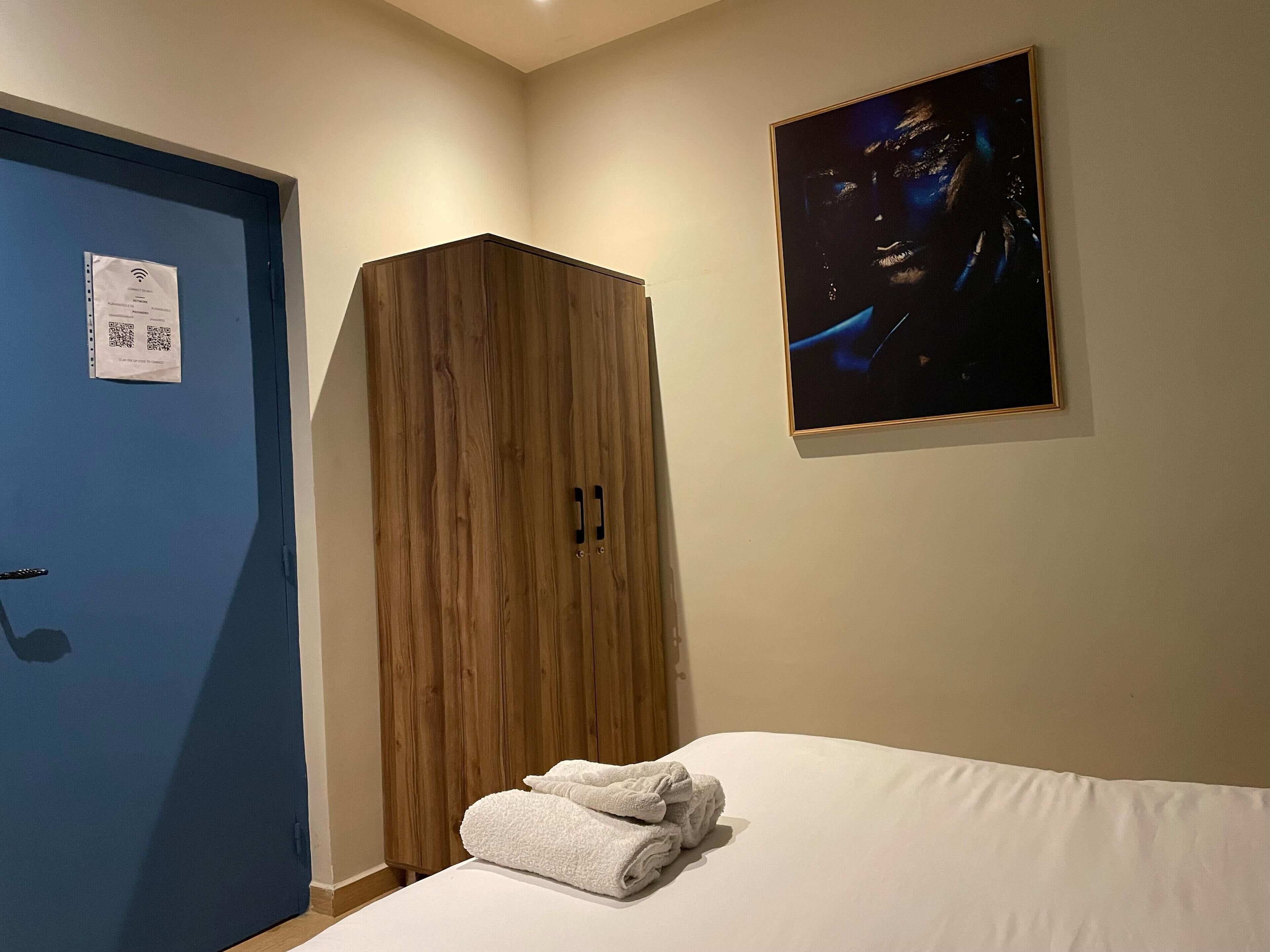 A bedroom with a bed, a blue door, a wooden wardrobe, and a framed picture on the wall.