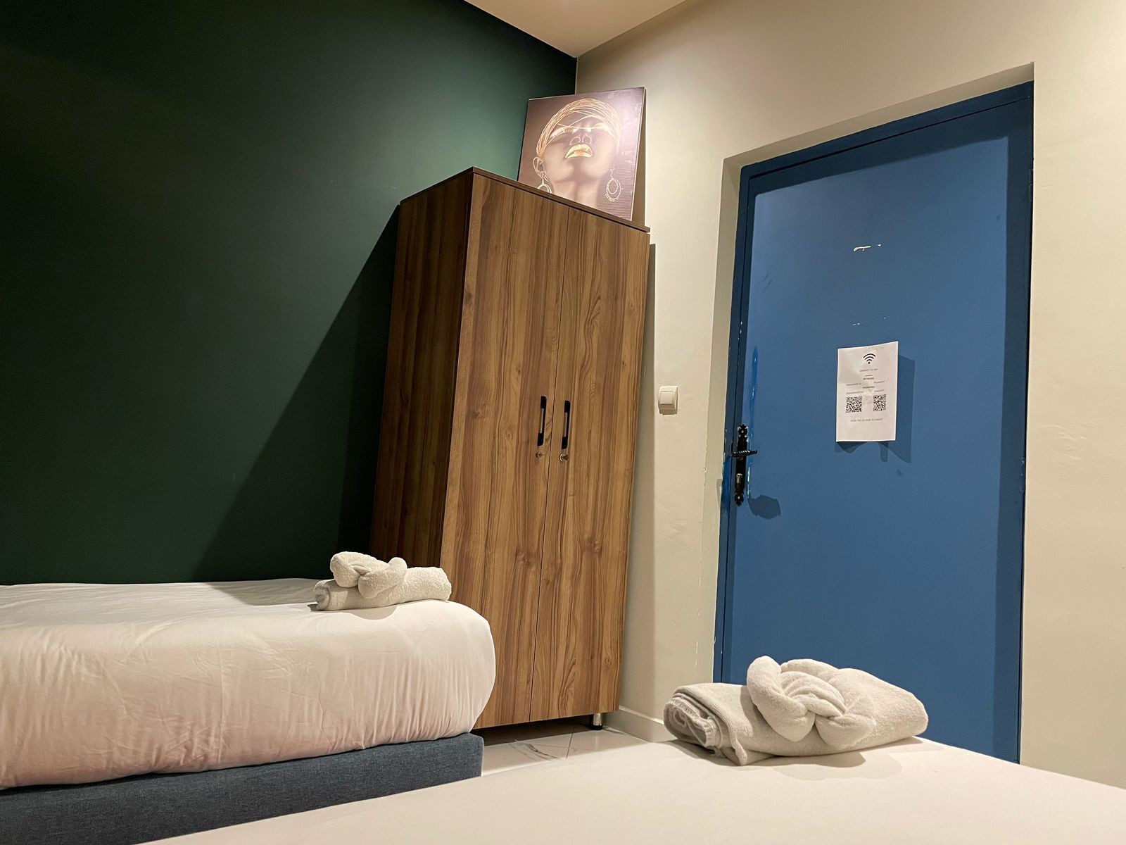 A bedroom with a bed, a wooden wardrobe, and a blue door.