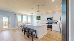 A modern kitchen with a central island, white cabinetry, stainless steel appliances, and a view to the outside. - 7 Day Weekend: 4  BR, 3  BA House in Crystal Beach, Sleeps 17 (Bolivar Peninsula)