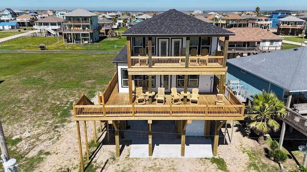 A two-story beachfront house with a balcony, outdoor seating, and a view of the ocean.