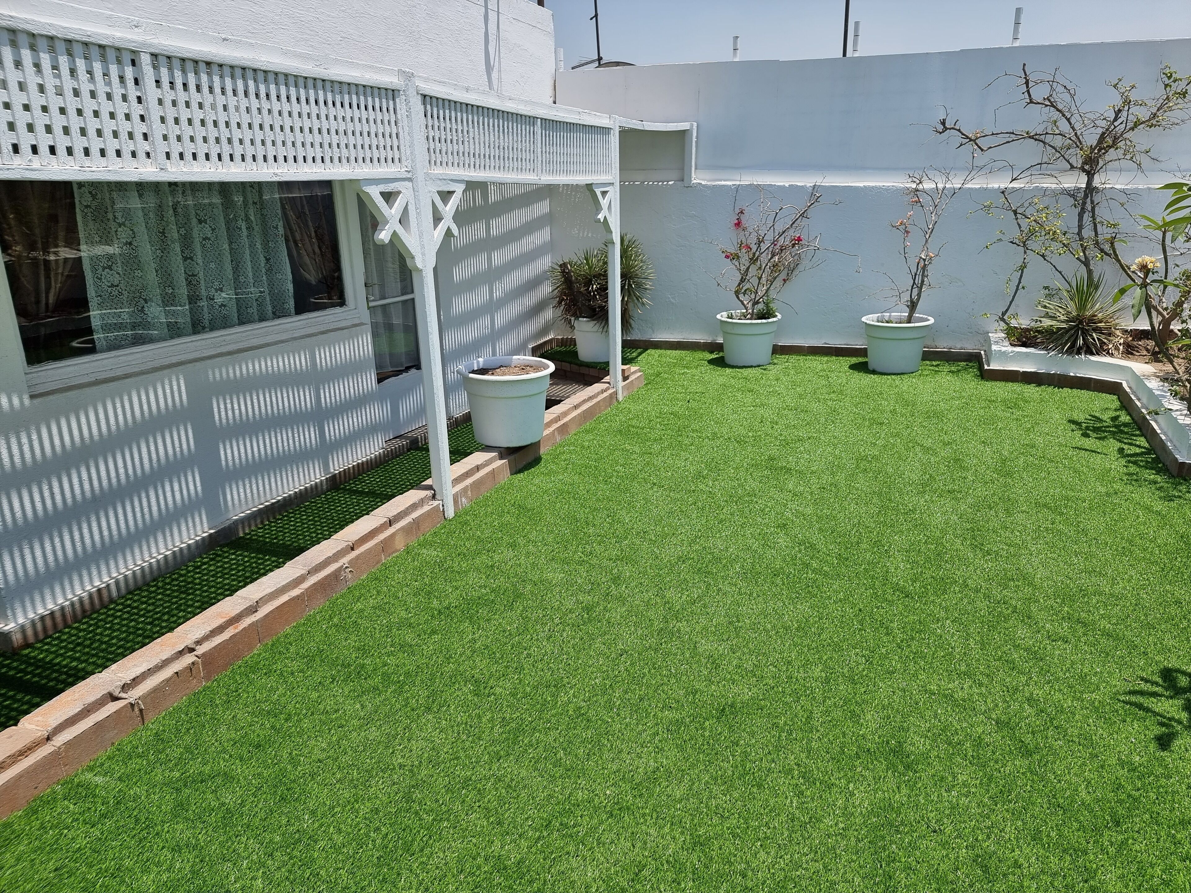 A well-maintained artificial grass lawn with white potted plants and a white fence.