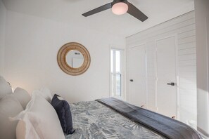 A bedroom with a bed, a ceiling fan, a round mirror, and a window. - Modern oceanfront condo - pool & playground - Incredible views! Linens included (North Topsail Beach)