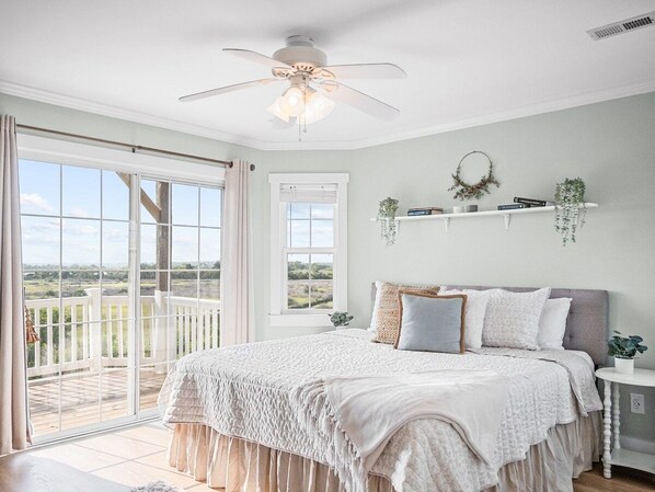 A bedroom with a large bed, a ceiling fan, and a balcony with a view. - Sound Front-Beach Access & Pool - Linens Included! (North Topsail Beach)