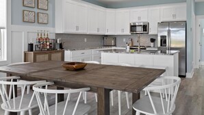 Une cuisine moderne avec des meubles blancs, une table à manger en bois et des chaises blanches.