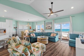 A spacious living room with a large sectional sofa, a round coffee table, and a view of the ocean through large windows. - Ocean views from every room w/ Elevator & Private Beach Access! Linens included (Surf City)