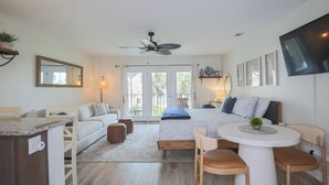 Een moderne slaapkamer met een bed, een plafondventilator, een televisie en een eethoek met een tafel en stoelen.
