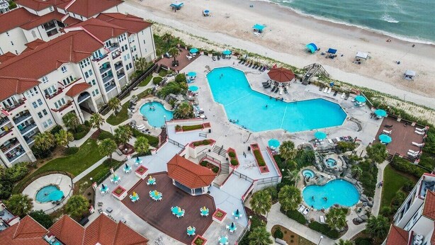 Luchtbeeld van een resort met meerdere zwembaden, een strand en een groot gebouw met balkons.