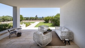 A patio with wicker furniture, a white sofa, and a view of a landscaped garden and sea. - Finamore - Panoramic villa with sea view, pool, forest, 4-5 bedrooms, Monopoli (Cozzana)
