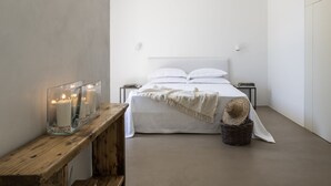 A minimalist bedroom with a large bed, bedside tables, a wooden bench, and a basket. - Finamore - Panoramic villa with sea view, pool, forest, 4-5 bedrooms, Monopoli (Cozzana)