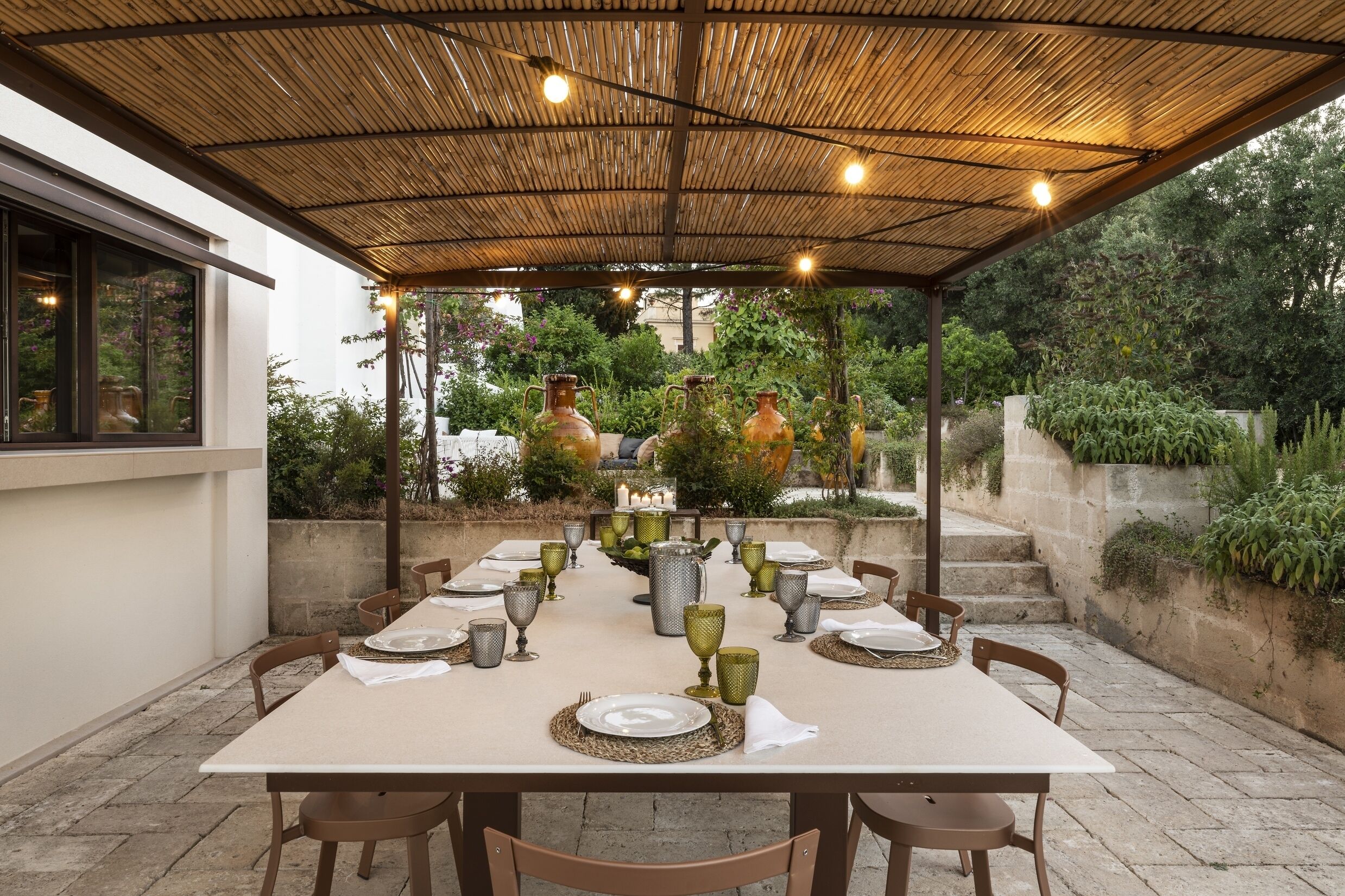 Un espacio comedor al aire libre techado, con una mesa lista para cuatro personas, rodeada de sillas.