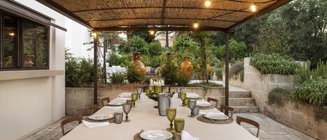 Un espacio comedor al aire libre techado, con una mesa lista para cuatro personas, rodeada de sillas.